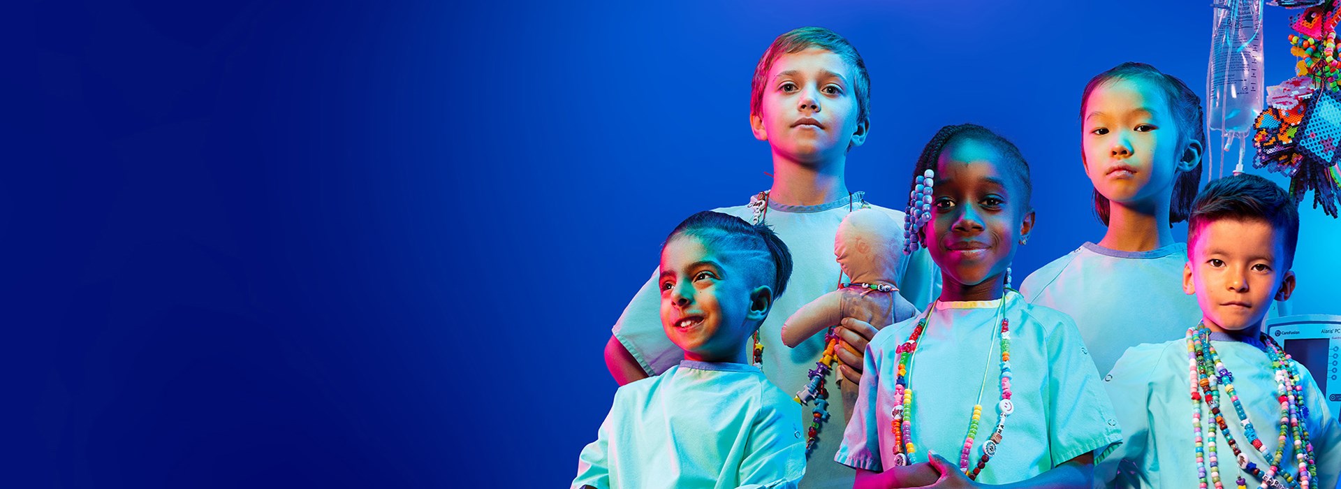Group shot of five SickKids Patients, various ages, genders and ethnicities. All in hospital gowns with three kids wearing their bravery beads.