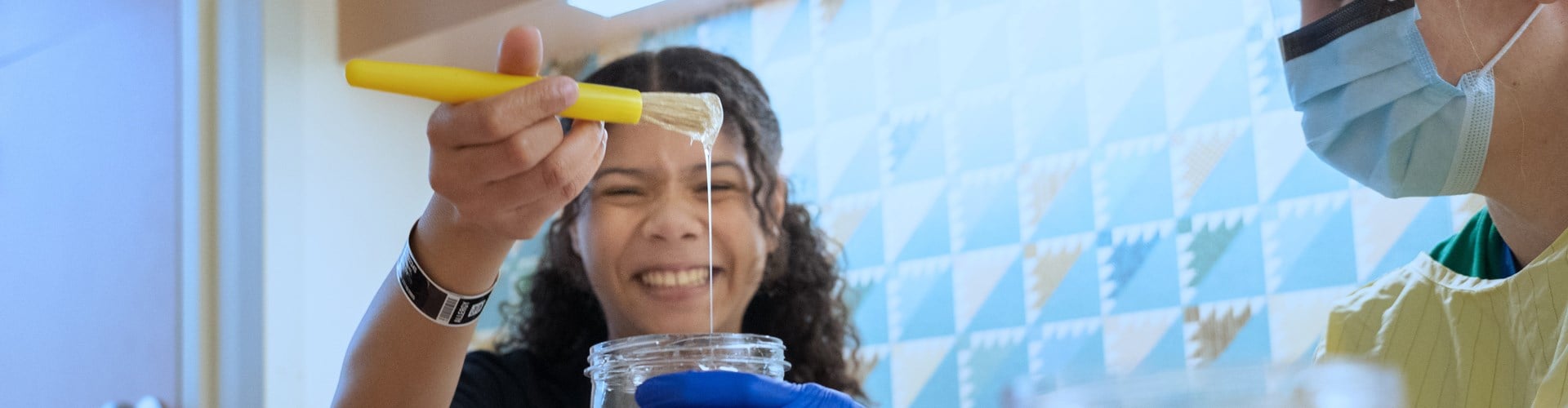 Girl scoops glue with a paint brush while a staff member helps