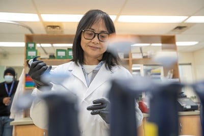 A lab professional wearing a lab coat and black gloves using a large pipette.